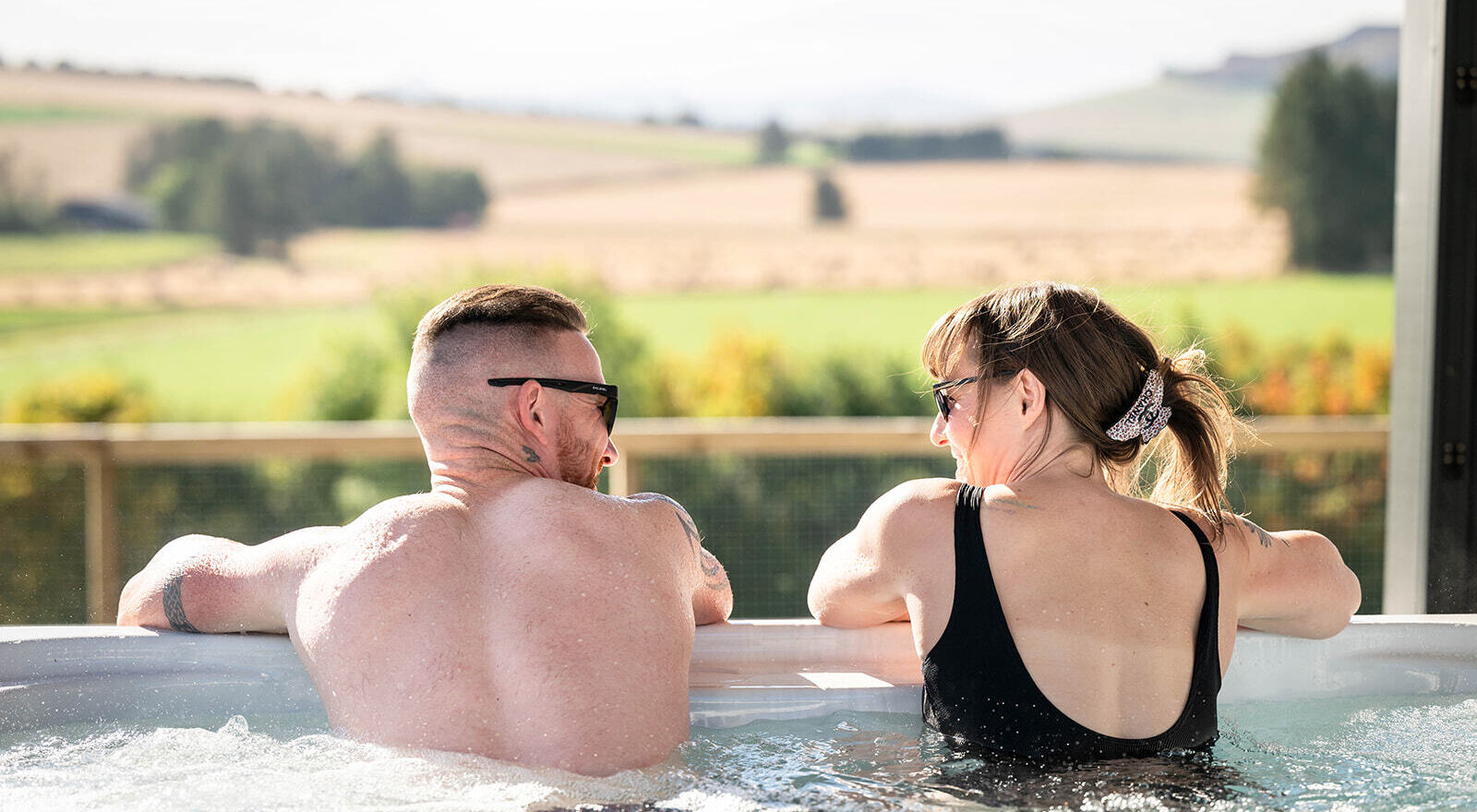 Couple relaxing in a private hot tub with views across the rolling Aberdeenshire countryside from a luxury lodge.
