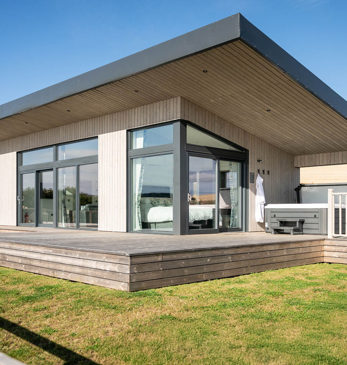 Exterior view of a modern luxury lodge with floor-to-ceiling windows, spacious decking, enclosed garden and private hot tub overlooking Aberdeenshire countryside.