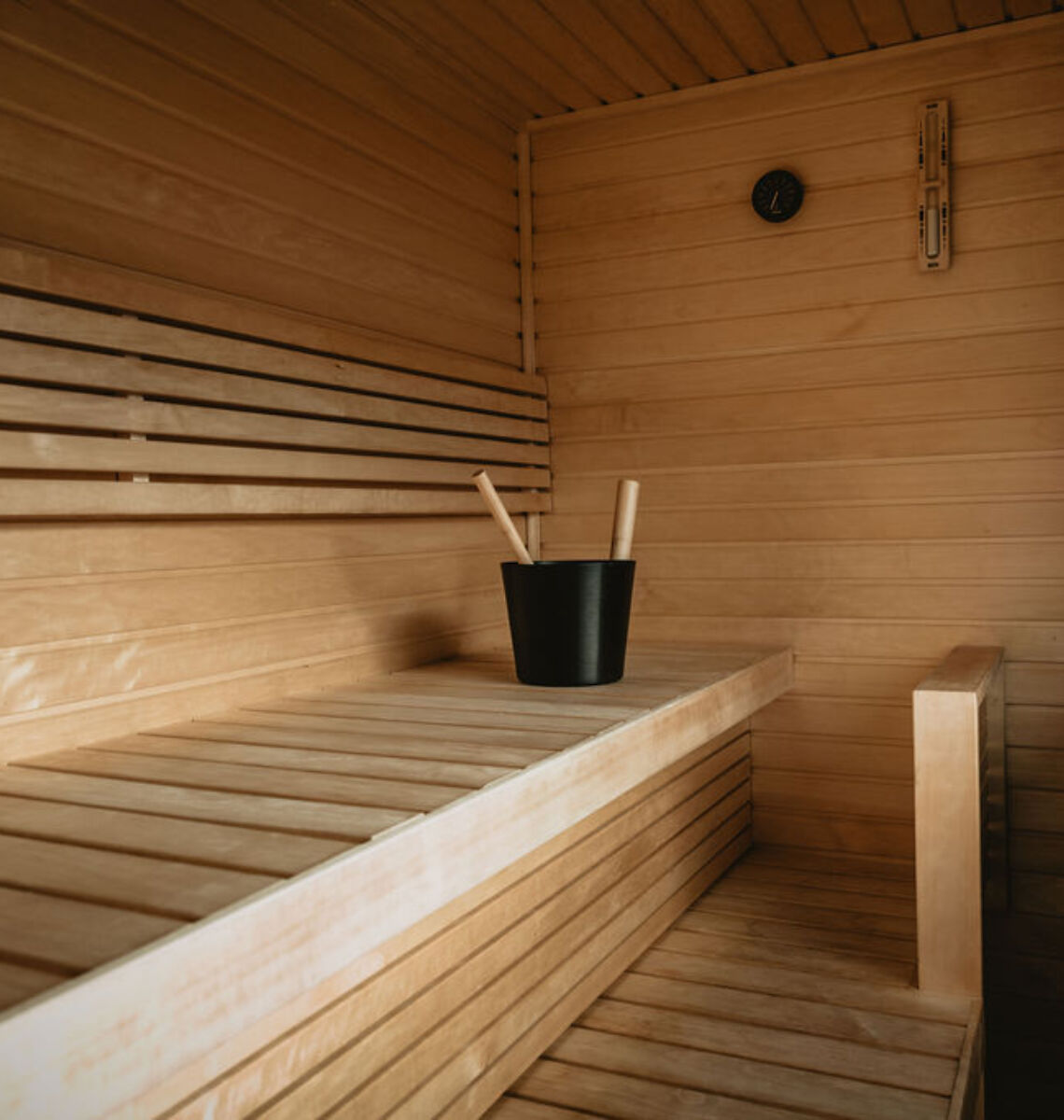 Interior of a wooden sauna with benches, a heater, and a bucket.