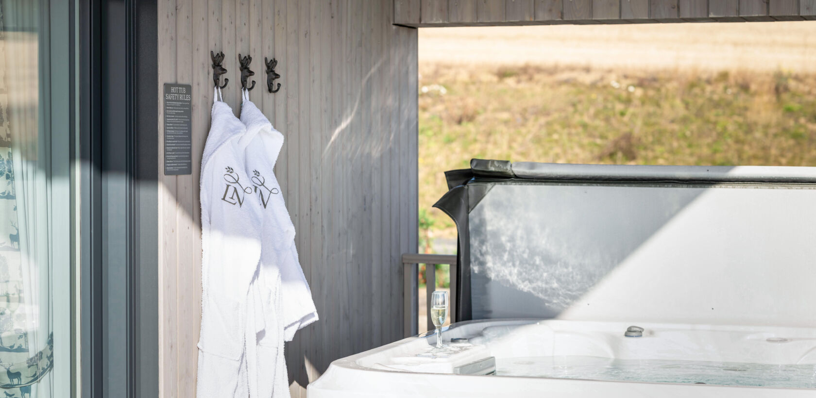 A hot tub outside a wooden structure with two white robes hanging on hooks nearby.