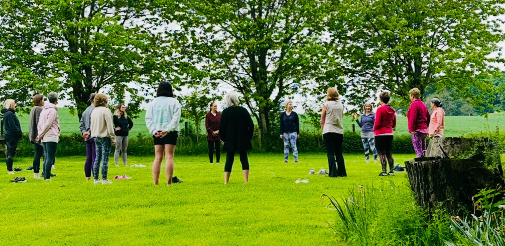 A group of people standing in a circle on a grassy area surrounded by trees.
