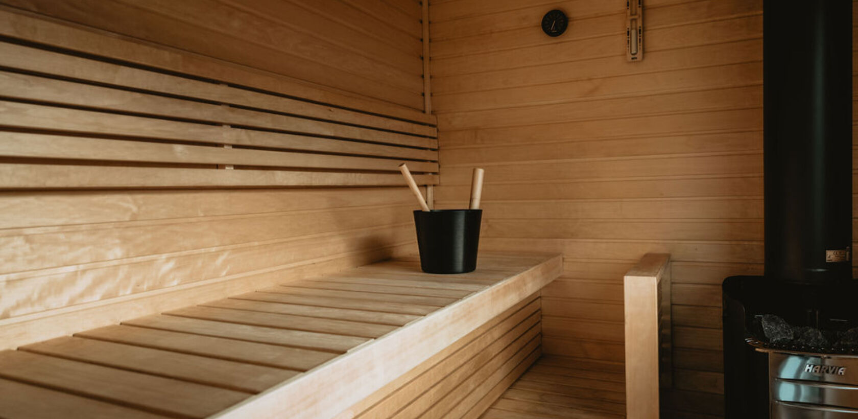Interior of a wooden sauna with benches, a heater, and a bucket.